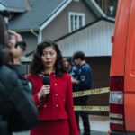 Female reporter in red with microphone reporting live at an outdoor crime scene with a news van.