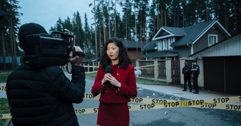 Journalist reporting live from a taped crime scene with cameraman and police.