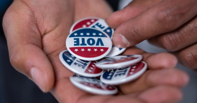 Close-up of hands holding patriotic voting pins representing democracy.