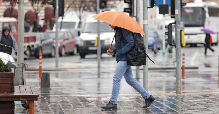 A man walks with an orange umbrella on a rainy day in Istanbul, Türkiye.