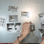 A handcuffed person examines evidence photos on a table, indicating a crime investigation scene indoors.