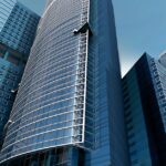 Futuristic urban skyscrapers with glass facades reflecting a vibrant blue sky.