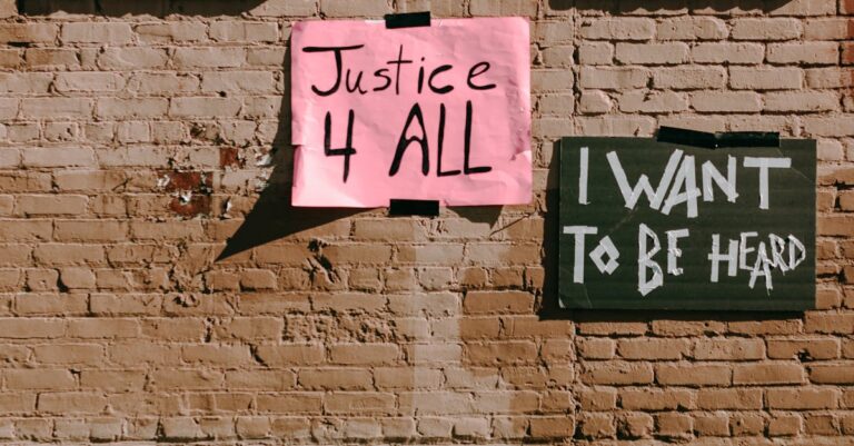Street activism signs on a brick wall promoting social justice and freedom of speech.