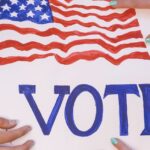 Hands arranging a patriotic voting poster with American flags, encouraging civic participation.