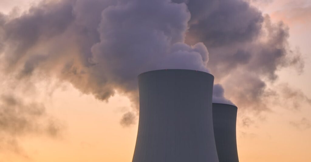 Silhouette of a nuclear power plant emitting steam during a colorful sunset.