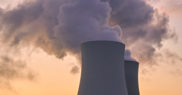 Silhouette of a nuclear power plant emitting steam during a colorful sunset.