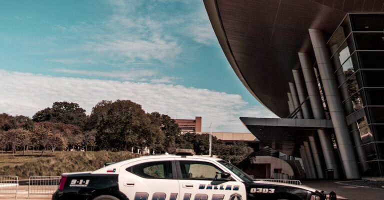 A police car parked outside a modern architectural building during the day with clear blue skies.