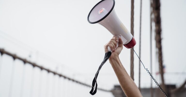 A hand holding a megaphone, symbolizing protest or announcement at an outdoor rally.