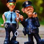 Two playful police figurines, complete with handcuffs and batons, depicted in a comical outdoor setting.