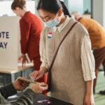 Voters casting ballots indoors on Election Day, wearing masks and using tablets for contactless voting.