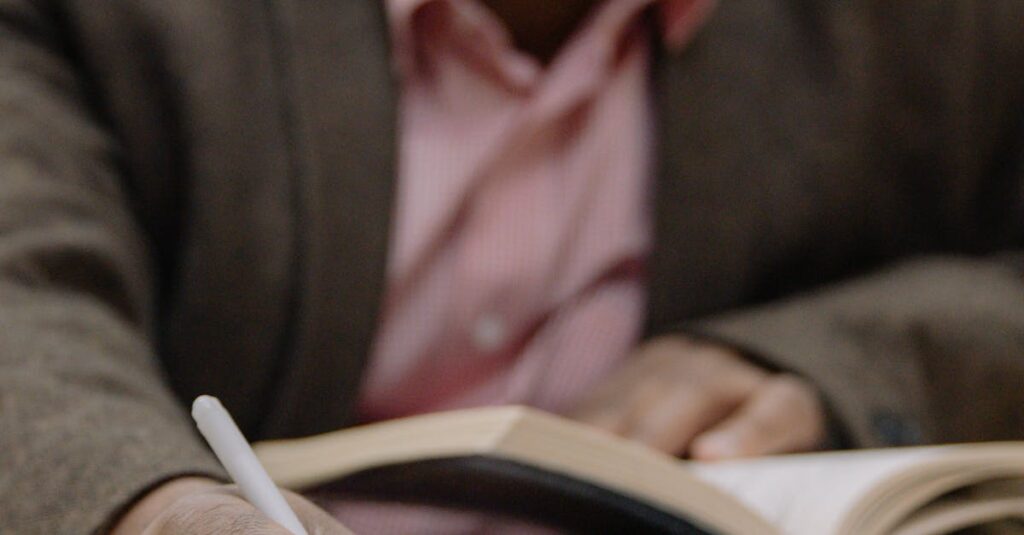 Adult man studying in a library, writing notes from an open book, with focus on hand and pen.