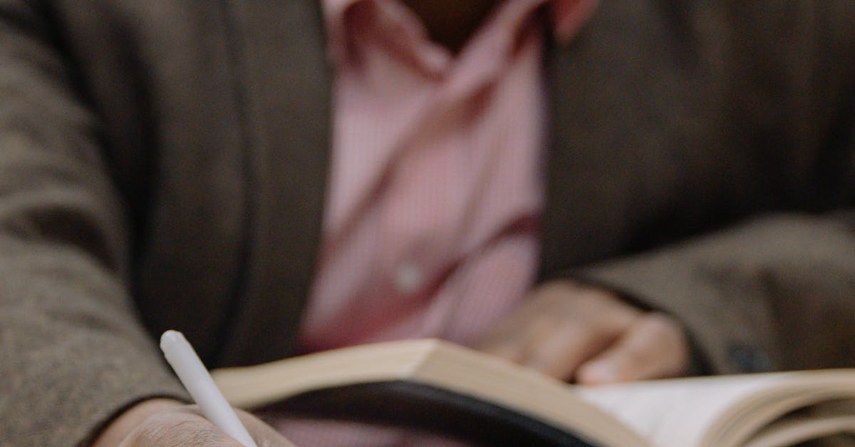 Adult man studying in a library, writing notes from an open book, with focus on hand and pen.