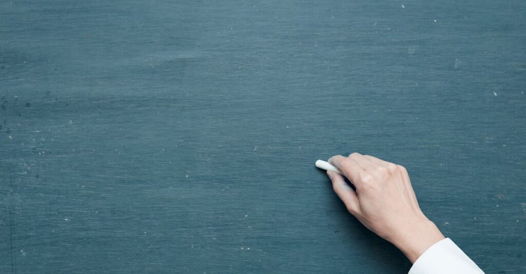 Hand holding chalk ready to write on a blank blackboard surface.