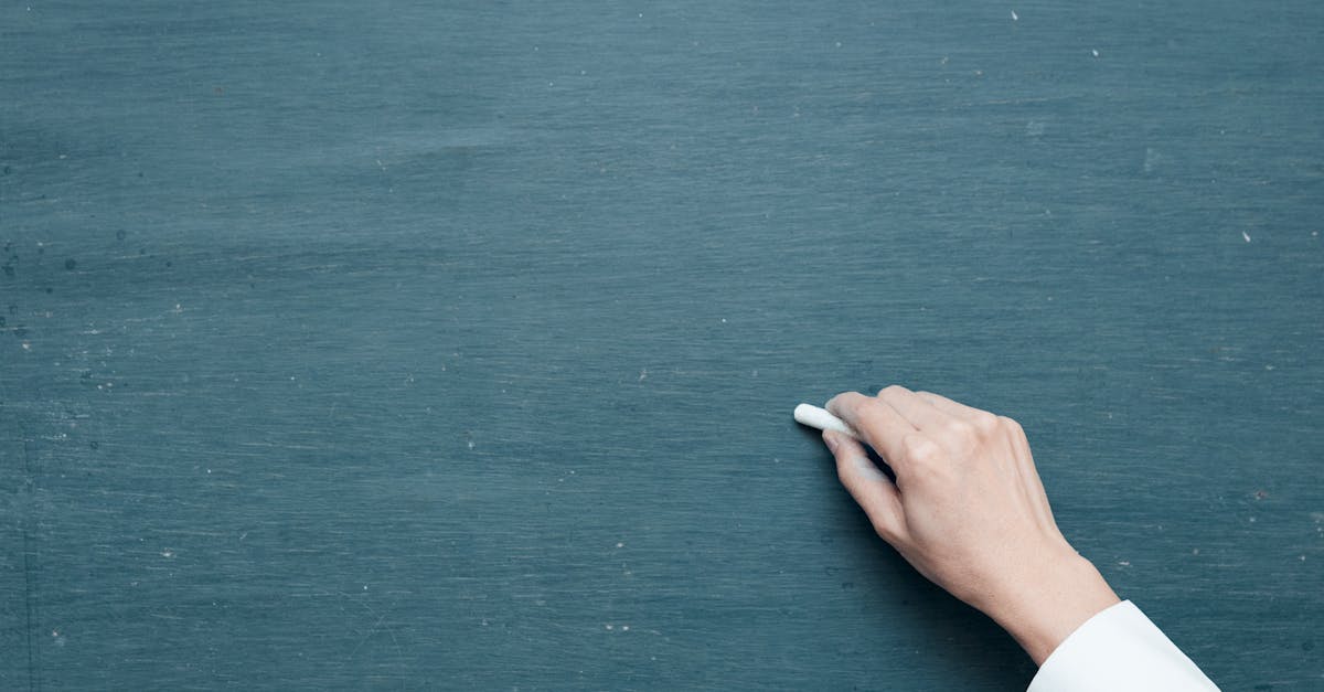 Hand holding chalk ready to write on a blank blackboard surface.