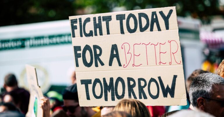 Crowd holding a protest sign with 'Fight Today for a Better Tomorrow', outdoors and during the day.