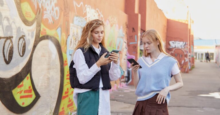 Two fashionable teenagers using smartphones in an urban graffiti setting, showcasing modern youth culture.