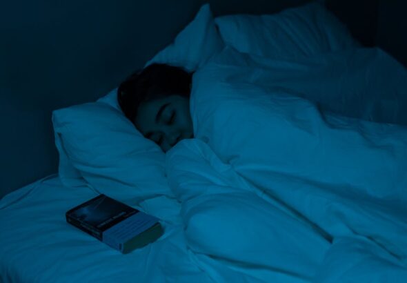 A woman peacefully sleeping with a book under blue night lighting, showcasing a cozy bedtime atmosphere.