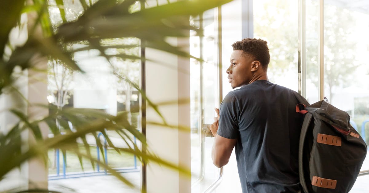 A college student with a backpack exits a campus building through glass doors.
