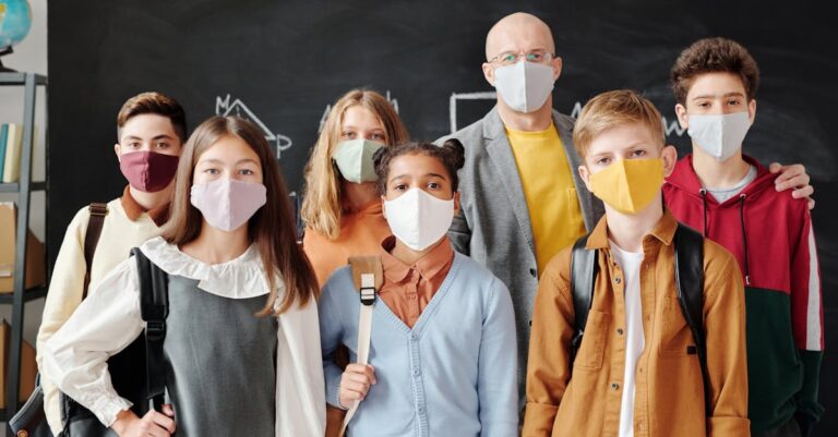 Group of students and a teacher in masks standing in a classroom during COVID-19 pandemic.