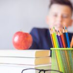 Schoolboy smiling behind a desk with books, pencils, and an alarm clock symbolizing study and creativity.