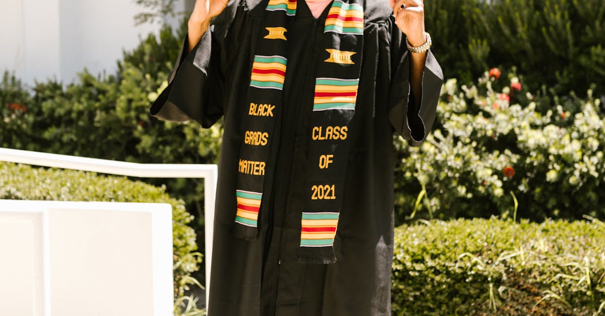 Smiling graduate wearing cap and gown celebrating outdoors with finger point gesture and colorful stole.