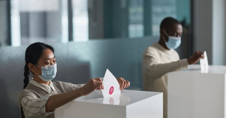 People casting ballots in an indoor election setting, practicing safety measures with masks.