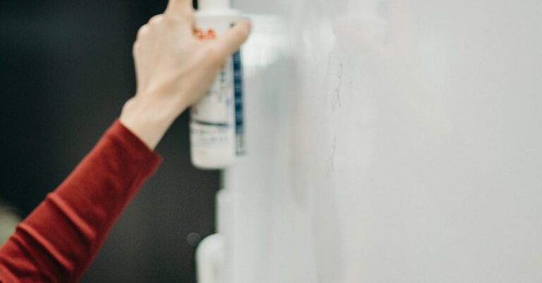 Close-up of hands cleaning a whiteboard with spray bottle in an office.