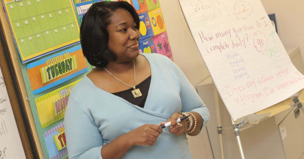 A female teacher standing by a whiteboard in a colorful classroom setting.