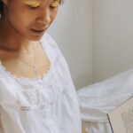A young woman with natural hair enjoys reading a book by the window with warm sunlight.