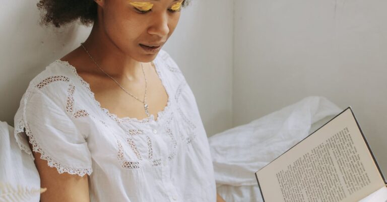 A young woman with natural hair enjoys reading a book by the window with warm sunlight.