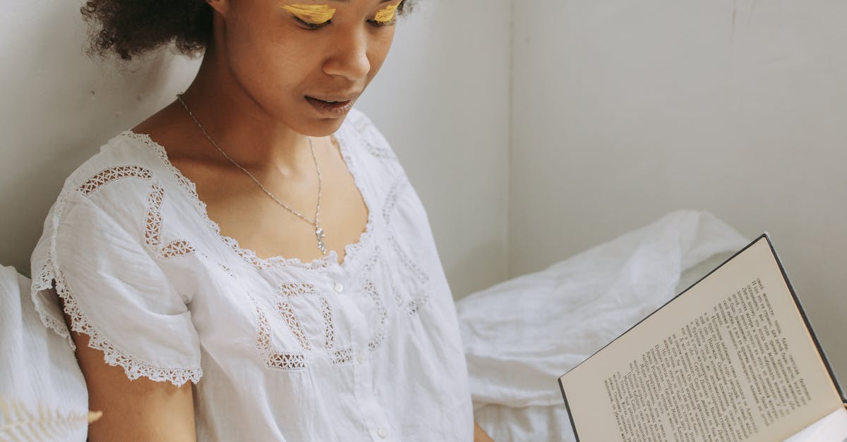 A young woman with natural hair enjoys reading a book by the window with warm sunlight.