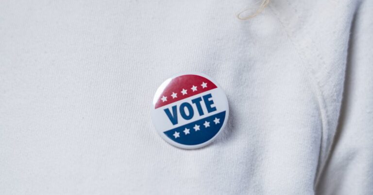 A close-up of a voter wearing a vote button on a white sweater, symbolizing civic duty.