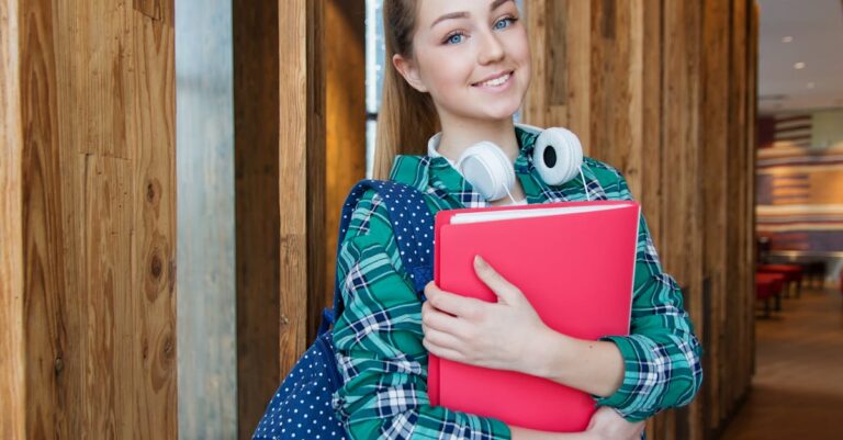 Smiling student holding book and wearing headphones, ready for study.