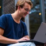 A young man sitting outdoors in Leiden, Netherlands, working on a laptop.