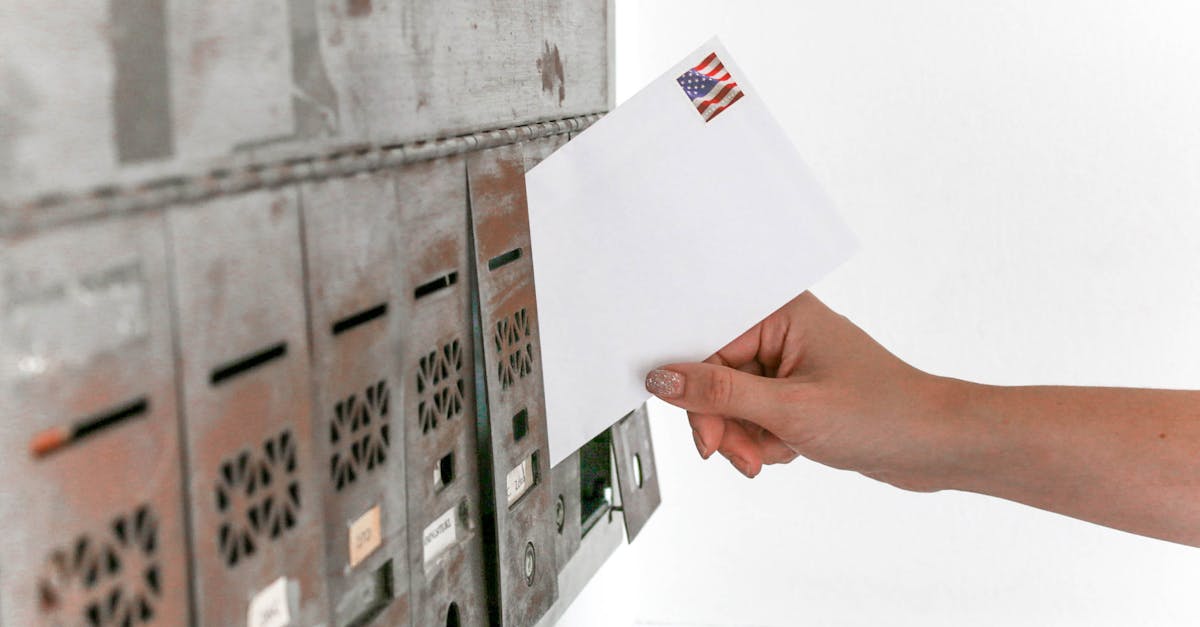 Close-up of a hand inserting a stamped envelope into a mailbox, symbolizing voting.