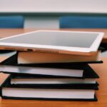 A tablet rests on top of a stack of books in an empty classroom, illustrating modern education.