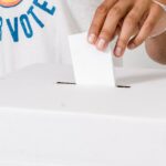 Close-up of a person placing a vote into a ballot box, highlighting voter participation.