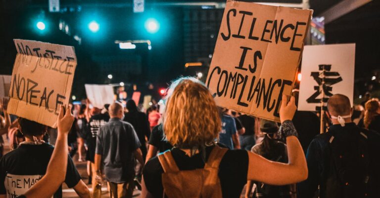 Activists gather at night for a protest in the city, holding signs and expressing their message.