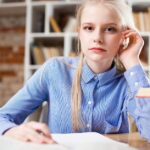 A young woman with blond hair studying at a table piled with books.