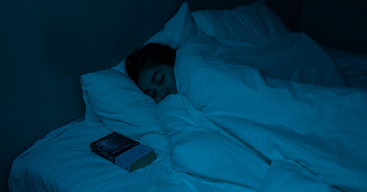 A woman peacefully sleeping with a book under blue night lighting, showcasing a cozy bedtime atmosphere.