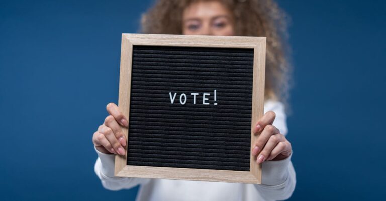 Woman holding a wooden framed board with 'Vote!' text, highlighting democratic participation.