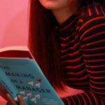 A woman lying on a pink background reading a book called 'The Making of a Manager'.