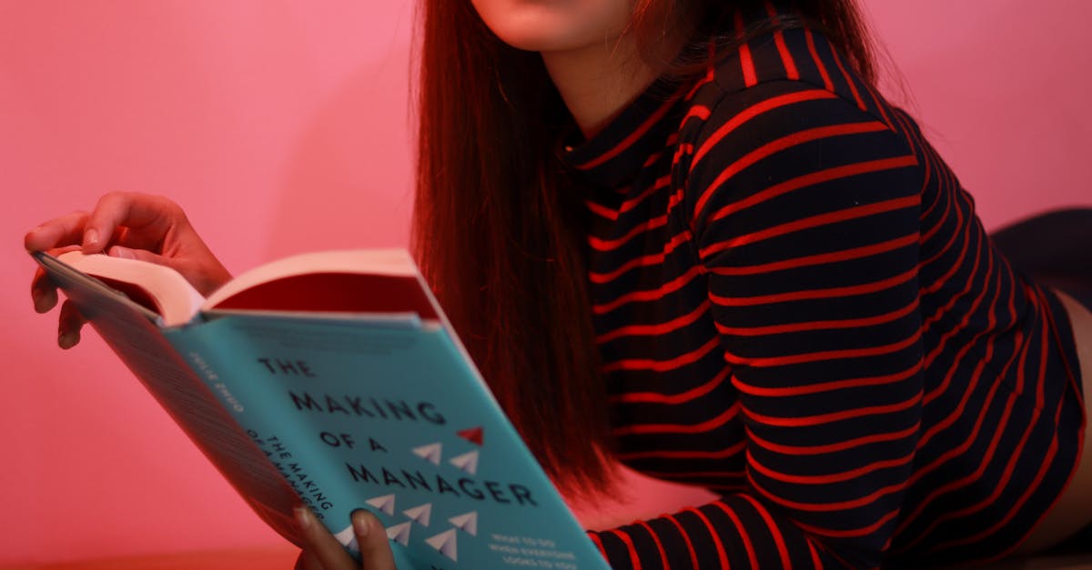 A woman lying on a pink background reading a book called 'The Making of a Manager'.