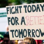 Crowd holding a protest sign with 'Fight Today for a Better Tomorrow', outdoors and during the day.