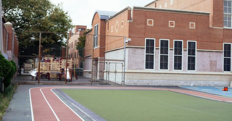 Empty urban schoolyard featuring a red brick building, playground, and athletic track, captured during daytime.