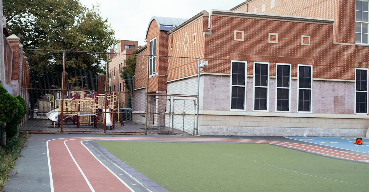 Empty urban schoolyard featuring a red brick building, playground, and athletic track, captured during daytime.