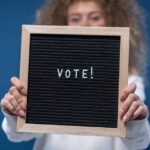 Woman holding a wooden framed board with 'Vote!' text, highlighting democratic participation.